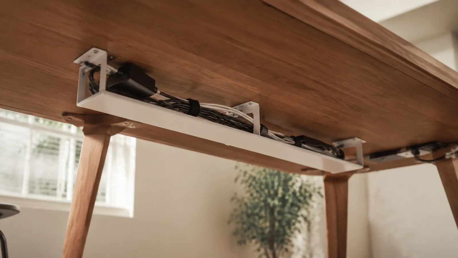 Clean home office desk from below showing cables neatly organized in a white under-desk tray, warm afternoon light