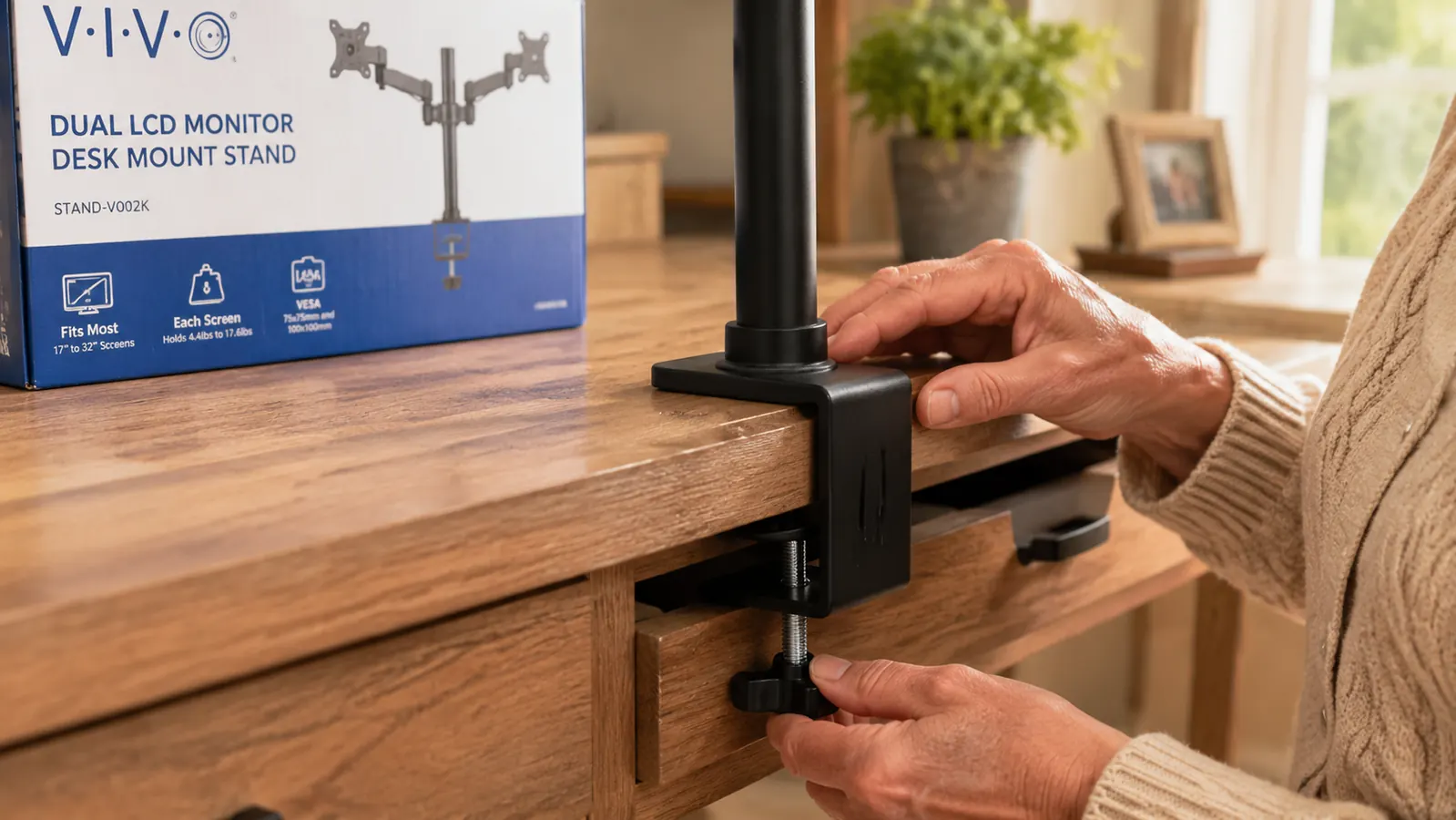 A c-clamp monitor mount base gripping the edge of a wooden desk, showing clearance between the clamp jaw and a desk drawer below