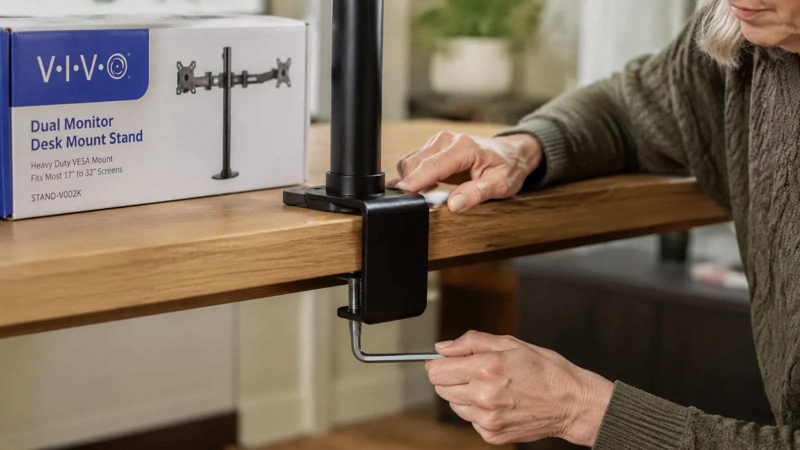 Close-up of a hand tightening the VIVO monitor mount clamp onto the back edge of a wooden desk
